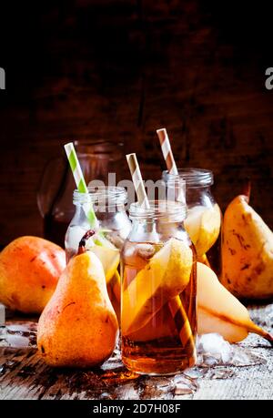 Jus de poire clarifié avec de la glace et des tranches de fruits dans des bouteilles de verre avec des pailles sur un fond en bois foncé, foyer sélectif Banque D'Images