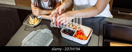 Fille regardant sa mère mettre de la nourriture dans sa boîte à lunch Banque D'Images