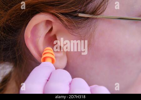 Une femme insère des bouchons d'oreille dans son oreille dans des gants médicaux de protection, en gros plan Banque D'Images