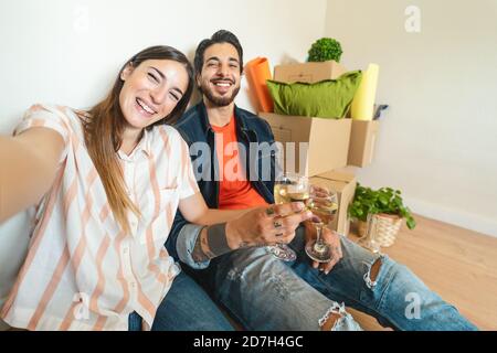 Un jeune couple heureux qui prend son selfie tout en célébrant avec du champagne à l'intérieur nouvelle maison pour la première fois Banque D'Images