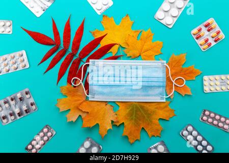 Masques médicaux bleus et feuilles sur fond vert, vue de dessus, automne en cas de pandémie. Banque D'Images