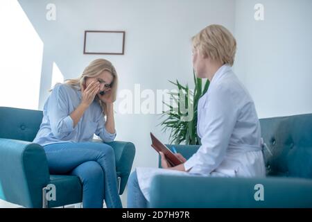 Patiente désespérée pleurant, assise en face d'une femme blonde mature médecin Banque D'Images