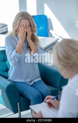 Inquiète femme patient couvrant son visage, assis en face de la femme médecin Banque D'Images