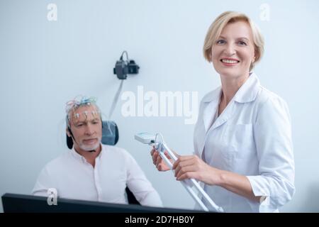 Lampe de retenue du neurologue féminin souriant, patient mâle subissant un électroencéphalogramme Banque D'Images