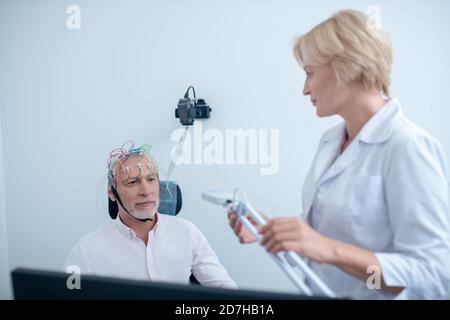 Lampe de retenue du neurologue féminin, regardant un patient mâle subissant un électroencéphalogramme Banque D'Images