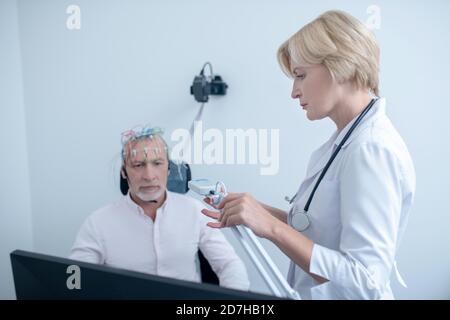 Neurologue féminin observant un patient mâle à cheveux gris sous électroencéphalogramme Banque D'Images