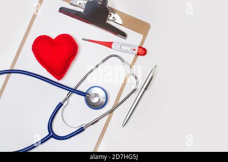 Un stéthoscope et un thermomètre sur un presse-papiers avec un coeur rouge en tissu Banque D'Images