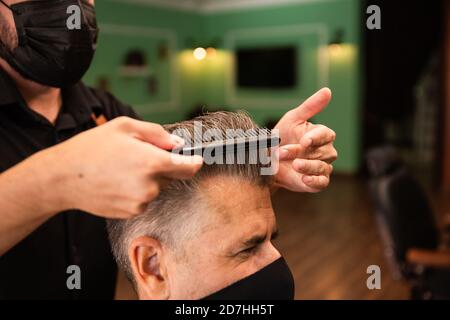 dans un salon de coiffure, un coiffeur peigne un grand homme avec sa main et son peigne, il porte des masques pour la prévention du coronavirus pandémique. le client est assis. hanches Banque D'Images