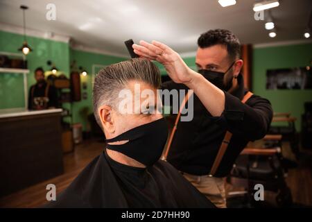 dans un salon de coiffure, un coiffeur peigne un grand homme avec sa main et son peigne, il porte des masques pour la prévention du coronavirus pandémique. le client est assis. hanches Banque D'Images