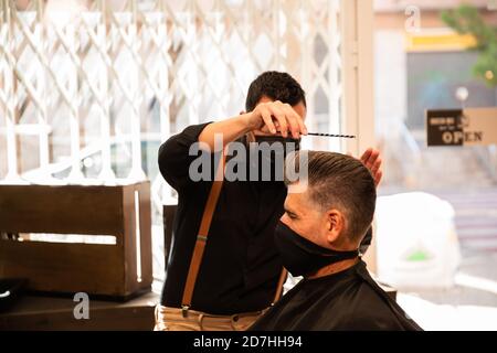 dans un salon de coiffure, un coiffeur peigne un grand homme avec sa main et son peigne, il porte des masques pour la prévention du coronavirus pandémique. le client est assis. hanches Banque D'Images