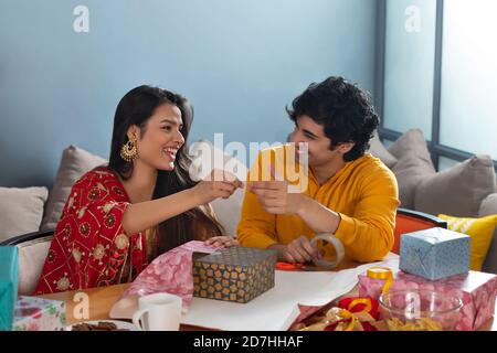 un jeune couple parle et se regarde les uns les autres tout en emballant un cadeau pour la fête de diwali Banque D'Images