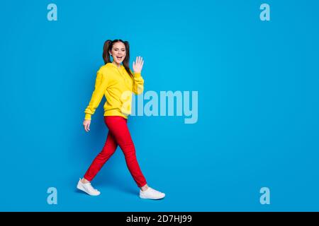 Pleine photo de profil de dame gaie deux queues bon mood walk street voir les amis se promener main porter décontracté jaune sweat à capuche rouge pantalon baskets Banque D'Images