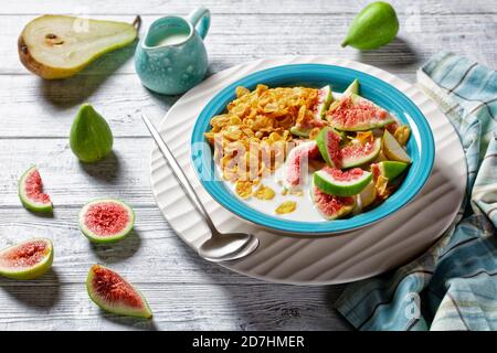 Bol bleu avec yaourt nature et croustillant aux cornflakes, figues, poire servi sur fond de bois blanc, vue du dessus, gros plan Banque D'Images