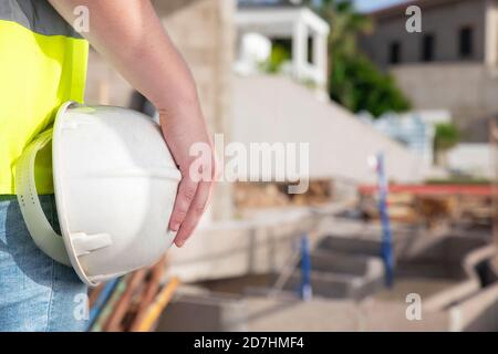 Main de l'architecte portant un gilet de sécurité et tenant un casque blanc, tout en se tenant sur le chantier d'une propriété privée, en surveillant Banque D'Images