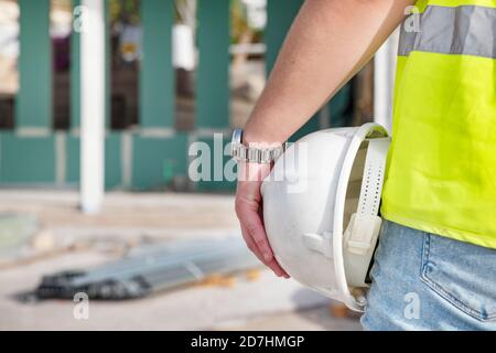 Gros plan de la main d'un architecte portant un gilet de sécurité et tenant un casque blanc, tout en se tenant sur le chantier de construction d'une propriété privée Banque D'Images