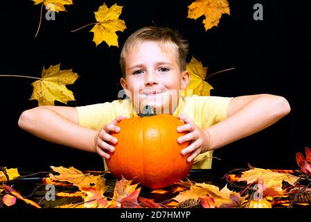 jeune garçon enfant enfant tenant la citrouille biologique naturelle dans les mains sur une table sombre avec des feuilles d'érable jaune, gros plan photos avec visage souriant Banque D'Images