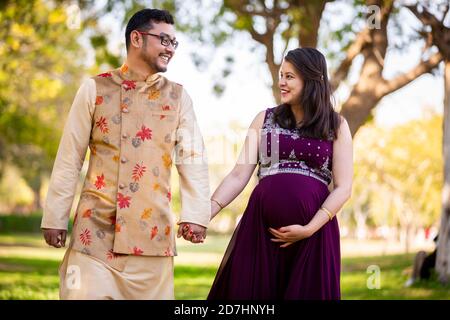 Bonne femme enceinte asiatique indienne avec son mari à marcher à l'extérieur dans un parc ou un jardin, souriant gai jeunes parents regardant l'appareil photo s'attendre Banque D'Images