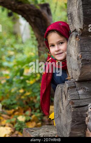 Une jeune femme dans un foulard russe traditionnel regarde autour du coin d'une maison en bois. Mouchoir Pavlovsk Banque D'Images