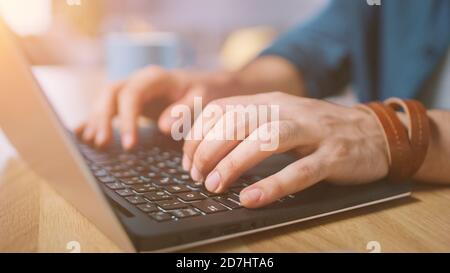 Gros plan d'un homme saisissant sur un ordinateur portable au bureau à domicile. Prise de vue avec lumière du soleil chaude. Banque D'Images