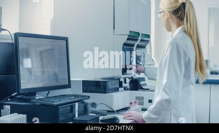 Scientifique de recherche féminine travaillant avec une machine d'analyse médicale pour tester les tubes avec échantillon de sang. Le scientifique travaille dans le secteur pharmaceutique innovant Banque D'Images