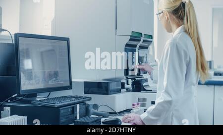 Scientifique de recherche féminine travaillant avec une machine d'analyse médicale pour tester les tubes avec échantillon de sang. Le scientifique travaille dans le secteur pharmaceutique innovant Banque D'Images