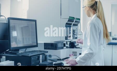 Scientifique de recherche féminine travaillant avec une machine d'analyse médicale pour tester les tubes avec échantillon de sang. Le scientifique travaille dans le secteur pharmaceutique innovant Banque D'Images