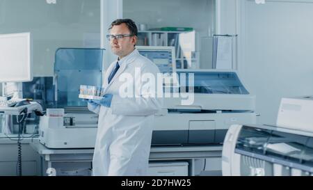 Un chercheur de sexe masculin fait le tour du laboratoire avec un plateau de tubes à essai rempli d'échantillons. Dans le laboratoire de travail de fond avec innovant Banque D'Images