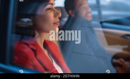 Belle femme et son partenaire masculin dans le siège arrière d'une voiture. C'est le soir dans la grande ville. Caméra prise de vue depuis l'extérieur du véhicule. Banque D'Images