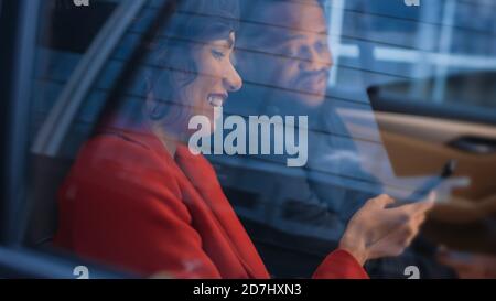 Belle femme et son partenaire masculin dans le siège arrière d'une voiture, ils partagent l'écran de smartphone et parler et Amuse-toi bien. C'est le soir dans le Grand Banque D'Images