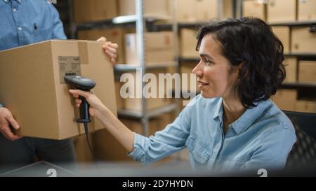 Le responsable des stocks de sexe féminin balaie la boîte en carton et, à l'aide d'un lecteur de code-barres, les employés masculins maintiennent le paquet. Dans les lignes de fond des boîtes en carton avec Banque D'Images