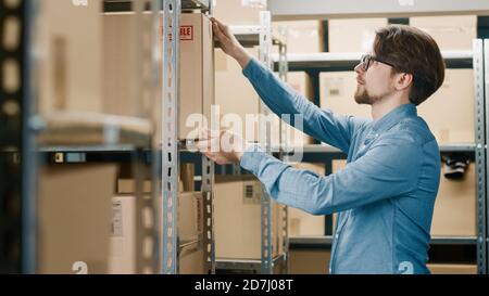 Un employé d'entrepôt dépose une boîte en carton sur une étagère. En arrière-plan, rangées d'étagères pleines de boîtes en carton et de colis remplis de produits prêts pour Banque D'Images