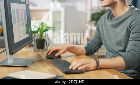 Gros plan de l'homme en utilisant l'ordinateur et ses mains en tapant sur un clavier et en utilisant la souris. Dans le salon confortable en arrière-plan. Banque D'Images