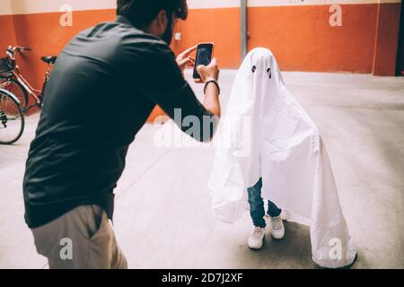 Père photographiant un enfant habillé comme un fantôme Banque D'Images