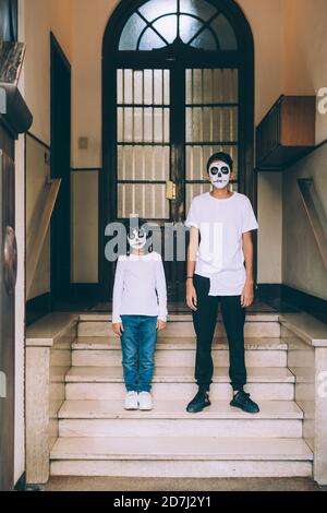 Soeur et frère dans la peinture de visage d'Halloween, debout sur les marches Banque D'Images