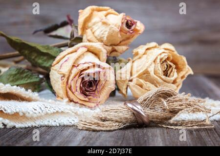 Anneaux de mariage et roses fleurs séchées sur fond de bois. Banque D'Images