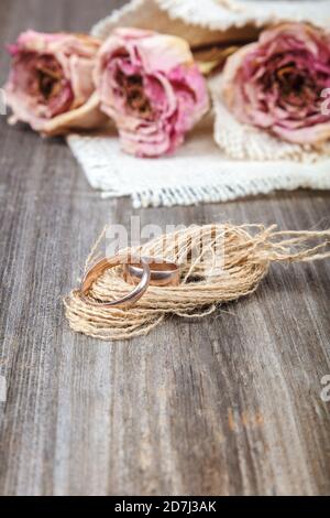 Anneaux de mariage et roses fleurs séchées sur fond de bois. Banque D'Images