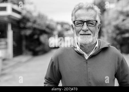 Joyeux homme barbu senior souriant en portant des lunettes et veste extérieure Banque D'Images