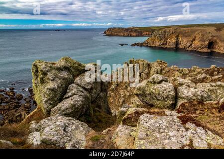 Vue côtière de Cornish en regardant vers le sud jusqu'à la fin des terres et au phare de Longships éloigné. Détail de la falaise de granit montrant l'érosion et les formes de roche couvertes de lichen Banque D'Images