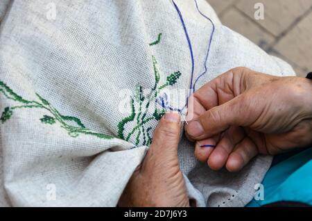 Mains d'une femme âgée broder un motif floral en point de croix sur du tissu en lin. Broderie, travail à la main, concept de l'aiguilleté. Gros plan Banque D'Images