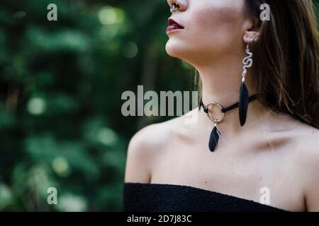 Jeune femme portant un collier et des boucles d'oreilles debout au parc Banque D'Images