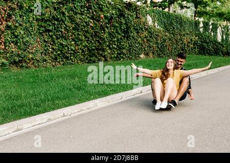 Des amis qui s'amusaient à faire de la planche à roulettes avec des bras étirés dans le parc Banque D'Images