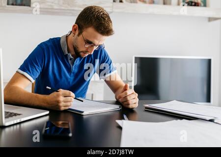 Un jeune étudiant fait des devoirs de mathématiques tout en étant assis à table Banque D'Images