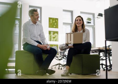 Des partenaires souriants utilisant un ordinateur portable lorsqu'ils sont assis au bureau Banque D'Images