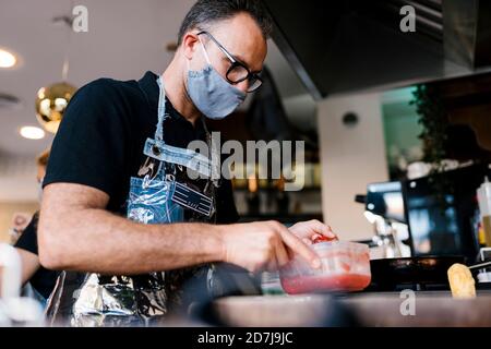 Un barista masculin portant un masque facial lors de la préparation des aliments dans un café Au cours de l'épidémie de COVID-19 Banque D'Images