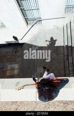 Guitariste jouant de la guitare tout en étant assis sur le mur de soutènement près de l'escalier en ville Banque D'Images