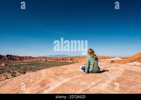 Femme assise sur la formation de roche au parc d'État de la Vallée de feu contre le ciel bleu, Nevada, États-Unis Banque D'Images