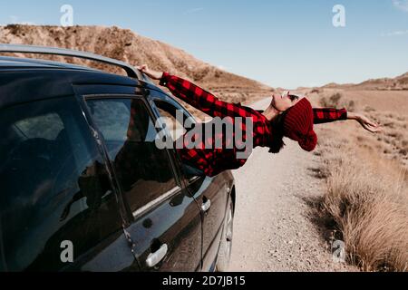 Espagne, Navarre, touriste féminine penchée hors de la fenêtre de voiture au-dessus de la route de terre dans Bardenas Reales Banque D'Images