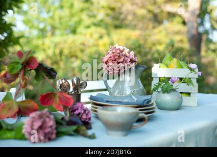 Vaisselle, abat-jour de lampe et verseuse avec hortensias en fleurs sur le café table dans le jardin Banque D'Images
