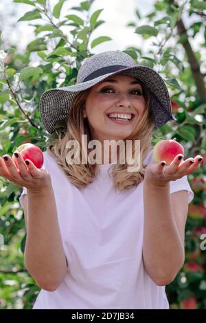 Femme joyeuse portant un chapeau tenant des pommes à la ferme Banque D'Images