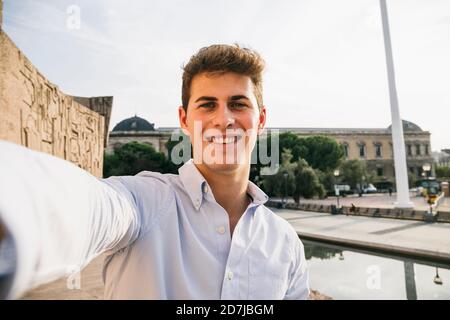 Un jeune homme souriant et charmant prend le selfie en ville contre le clair ciel Banque D'Images